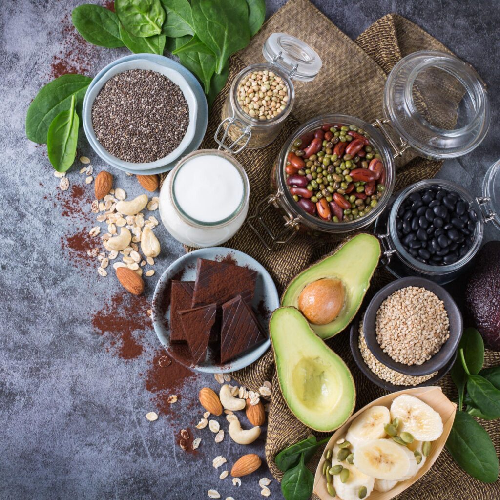 A top-down arrangement of healthy ingredients including dark chocolate, avocado, oats, yogurt, spinach, and various seeds and legumes in bowls and jars.